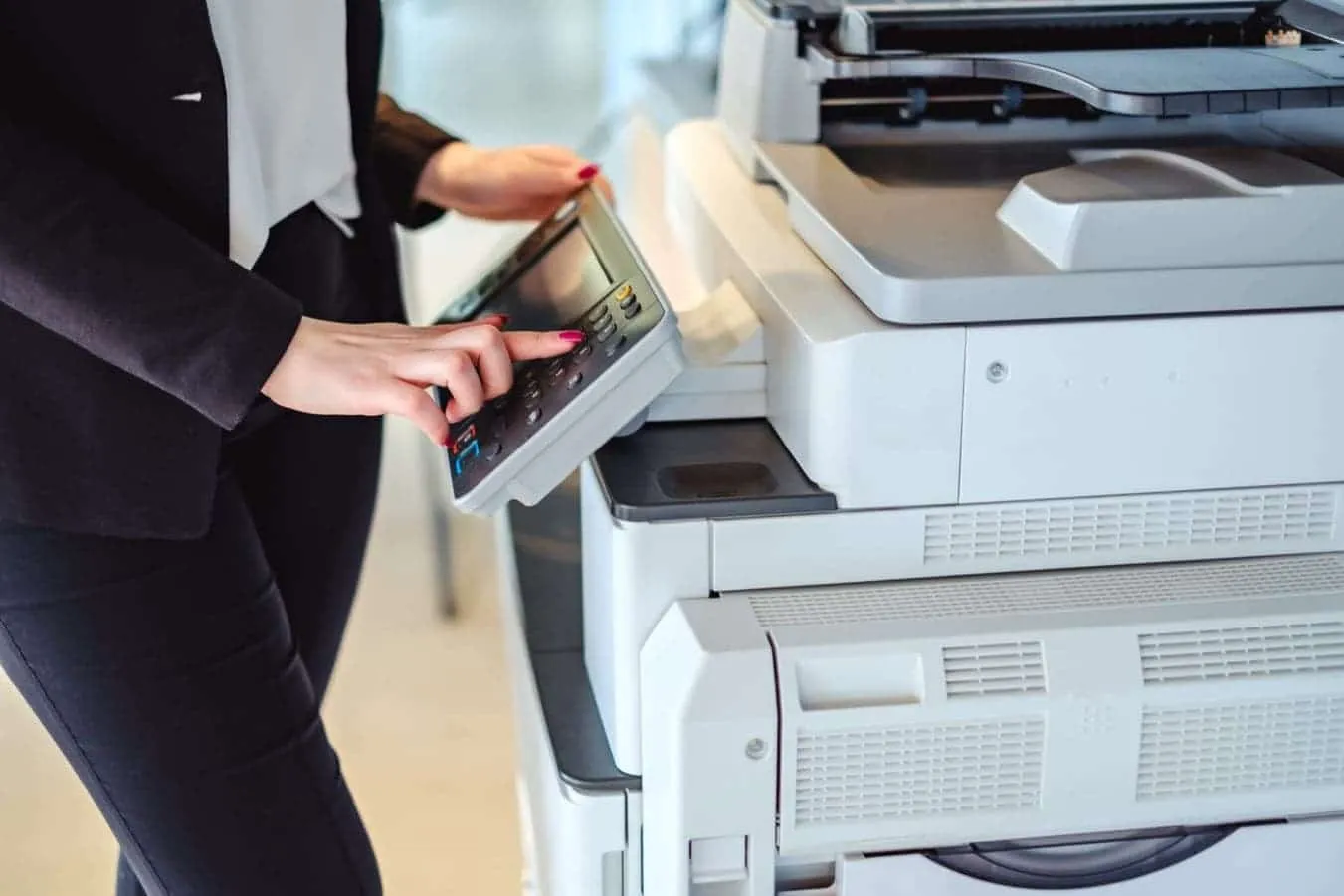 User operating a multifunction copier machine in an office setting, selecting options on the touchscreen panel.