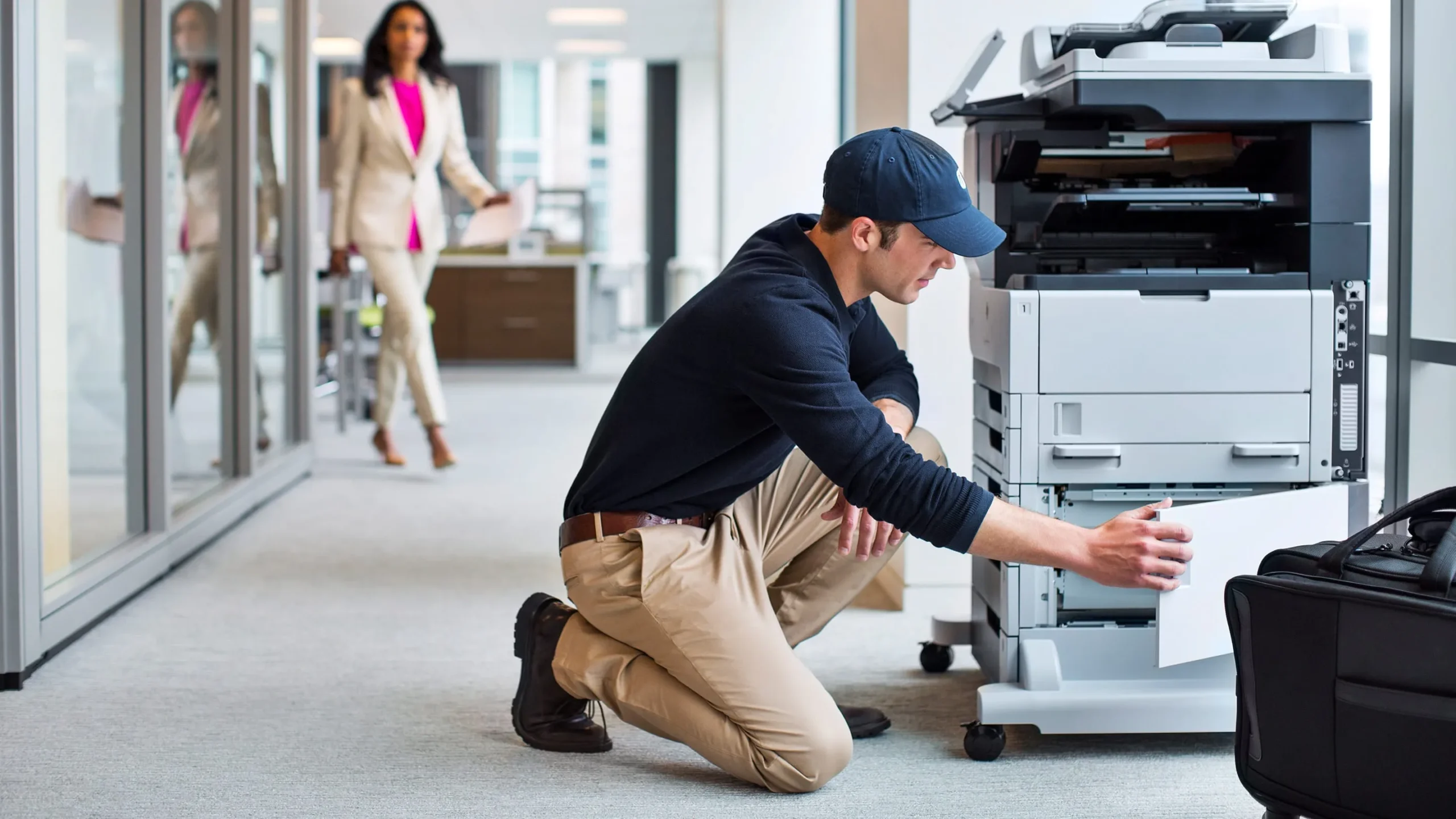 Technician performing copier repair services on a multifunction printer in an office setting, troubleshooting paper jam issue.