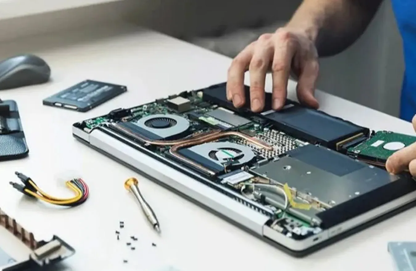 Technician repairing a laptop by replacing internal components, including the hard drive and cooling system.