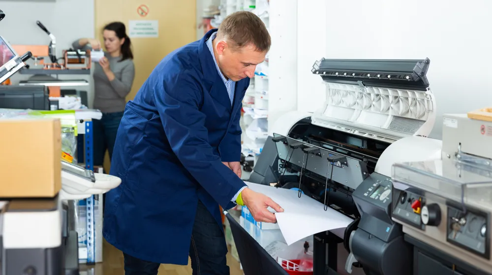Technician performing maintenance on a designjet printer repair, inspecting print quality and making adjustments in a printing workshop.