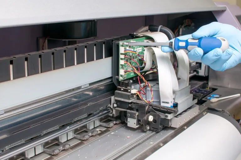 Technician performing designjet plotter repair on an HP large format printer, working on internal components with a screwdriver.
